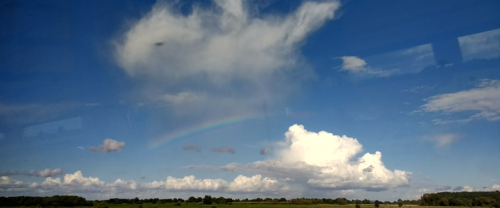 A photo snapped on the train in England which shows the full cycle of convective clouds. On the right is a developing clouds which is raining out, rapidly growing vertically. And on the left are remnants of an old convective cloud, evaporating into thin whisps of moisture which are caught by the sun's rays and create a rainbow.